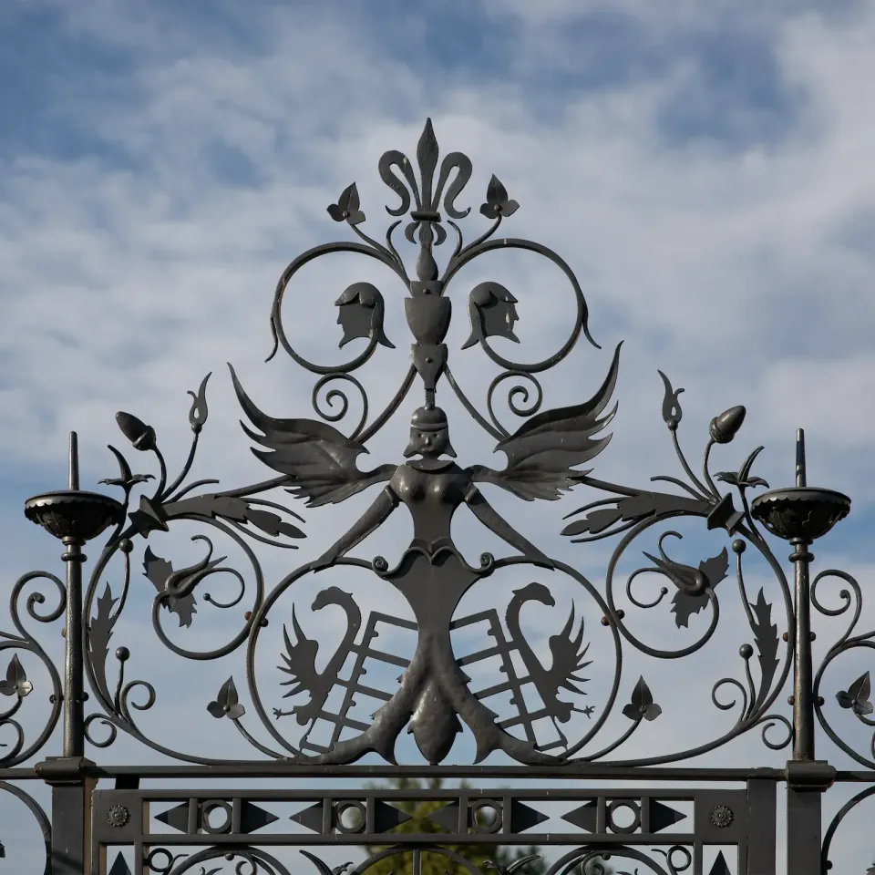 Aufsatz des Schmiedezauns mit Rankenwerk vor Wolkenhimmel